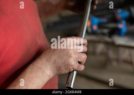 Tuyau en acier en main. Petit diamètre de profil en acier. Un homme tient un tube métallique dans l'atelier. Travail dans le garage en détail. Banque D'Images