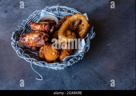 Nourriture dans le panier en osier sur la table. Oignons frits, ailes de poulet et boulettes de viande. Délicieux et savoureux. Banque D'Images