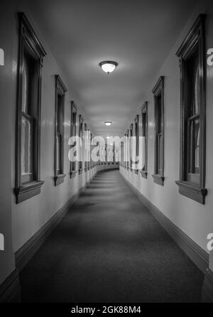 Prise de vue en niveaux de gris d'un long couloir lumineux avec fenêtres Banque D'Images