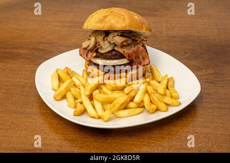 Double hamburger de bœuf avec cheddar, fromage de chèvre, cornichons marinés, tranches de bacon et compote de champignons avec frites Banque D'Images