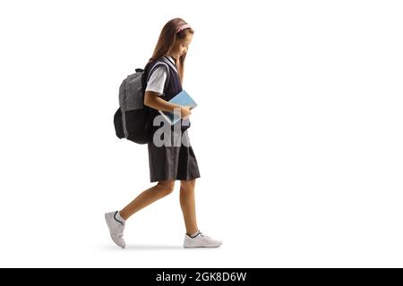 Plan de profil complet d'une jeune femme triste dans un uniforme scolaire marchant et tenant un livre isolé sur fond blanc Banque D'Images