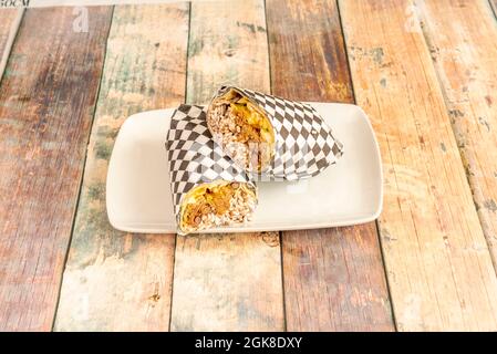 Burrito mexicain avec riz blanc, ragoût de haricots, laitue avec condiments et tortilla de blé enveloppée dans du papier alimentaire à carreaux Banque D'Images