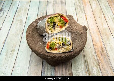 Grand burrito, divisé en deux, enveloppé dans du papier aluminium, farci de chorizo vert, haricots noirs, et de riz au fromage sur la pierre volcanique molcajete Banque D'Images
