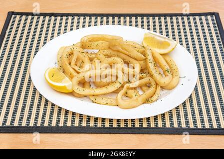 Plateau blanc sur une nappe en bambou roulante avec une généreuse portion d'anneaux de calmars battus et accompagné de quartiers de citron Banque D'Images