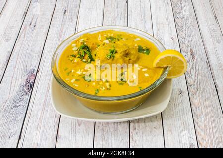 Grand bol rempli de bouillon de boules typiquement latino-américain avec agrumes et persil sur une table blanche Banque D'Images