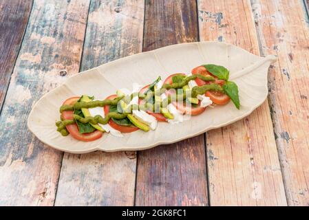 salade de caprese avec fromage de buffle, tomates, avocat et basilic et beaucoup de sauce pesto sur une assiette en forme de feuille Banque D'Images