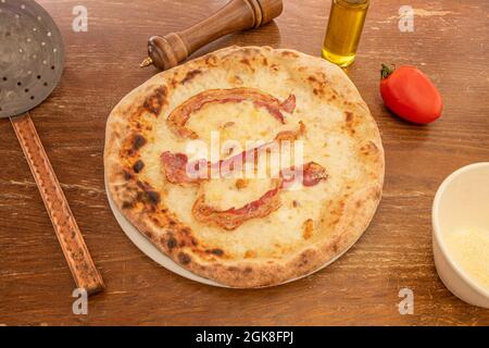 Pizza carbonara cuite dans le restaurant italien avec des tranches de bacon frit et du fromage fondu fait avec de la pâte de farine de blé sur une table en bois avec des ustensiles et Banque D'Images