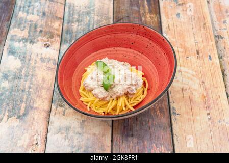 Bol rouge avec recette italienne pour spaghetti frais et sauce carbonara au basilic Banque D'Images