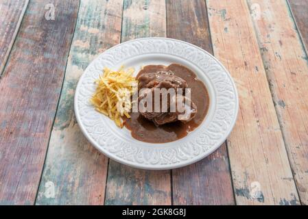 Les joues de porc ont mijoté avec une délicieuse sauce et des pommes de terre de paille sur une belle assiette blanche Banque D'Images