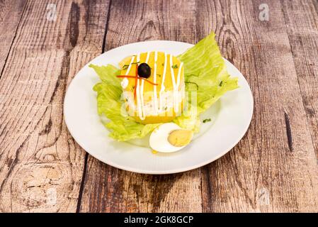 Typique péruvienne Causa Limeña présenté en couches avec des pommes de terre jaunes et de la salade de remplissage avec de la mayonnaise, des oeufs durs et des légumes sur une assiette blanche Banque D'Images