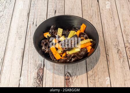 Salade chinoise épicée avec légumes, champignons et bambou dans un bol noir sur une table blanche Banque D'Images