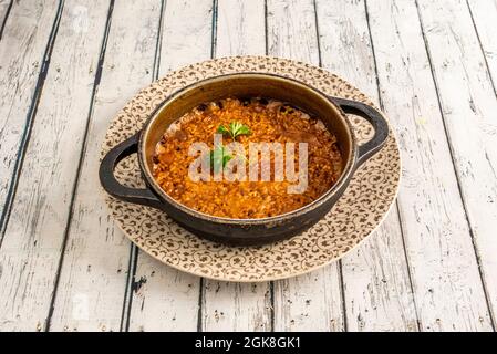 Paella de riz à la seiche servie dans une poêle en métal noir sur une table en bois blanc. Banque D'Images