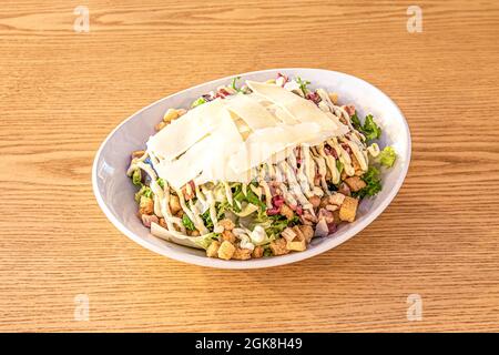 Salade César typique avec laitue, parmesan et mayonnaise avec persil sur un bol blanc et une table en chêne Banque D'Images