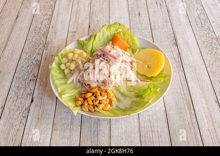 Généreuse portion de ceviche de poisson péruvien avec oignon rouge, pomme de terre cuite, porc, patate douce et laitue sur une assiette blanche Banque D'Images