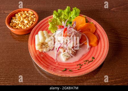 Jolie assiette rouge avec ceviche de poisson de style péruvien avec du maïs blanc, du cancha et des tranches de patate douce sur une table en bois sombre Banque D'Images