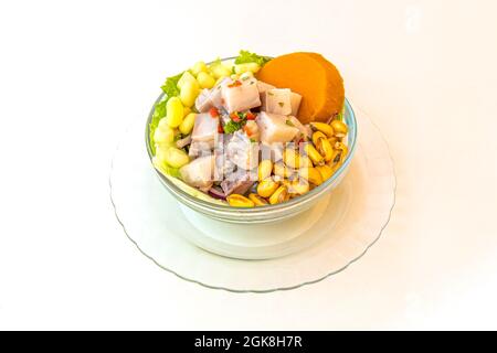 Bol en verre rempli de ceviche de poisson péruvien avec du cancha, de la patate douce et de la laitue sur fond blanc. Banque D'Images