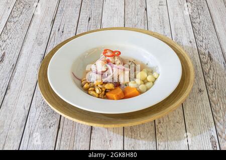 Ceviche péruvienne typique de bar mariné avec des oignons rouges, des poivrons, de la lime, du cancha, de la ciboulette et de la patate douce sur une assiette blanche profonde Banque D'Images