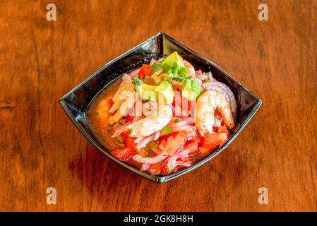 Ceviche dans un bol noir avec une généreuse portion de crevettes, tomate, avocat, persil et oignon rouge Banque D'Images