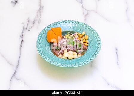 Ceviche de thon rouge avec tous les condiments typiques de ceviche de poisson péruvien avec pousses et coriandre à l'intérieur d'une belle assiette bleue sur un t de marbre blanc Banque D'Images