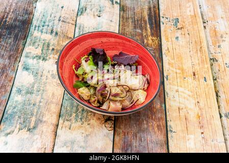 Ceviche au bar avec oignon rouge haché et pousses tendres de laitue dans un bol rouge sur une table en bois Banque D'Images