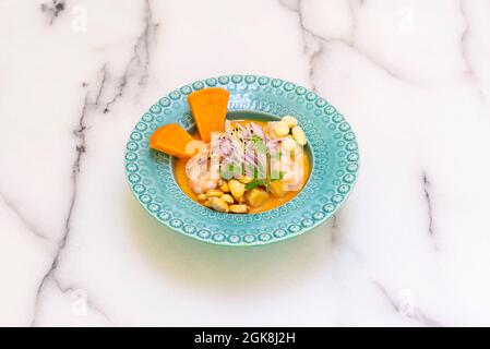 Mélange de bar de mer et de ceviche de crevettes avec de la patate douce marinée et du maïs sur une assiette bleue profonde sur une table en marbre Banque D'Images