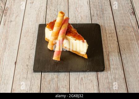 Portion de cheesecake avec confiture sur le dessus et gaufres aromatisées sur une assiette en ardoise noire Banque D'Images