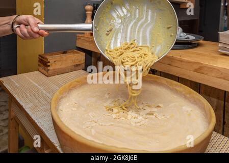 Un homme verse des spaghetti gras dans une poêle sur un demi-fromage grana padano dans un restaurant italien Banque D'Images