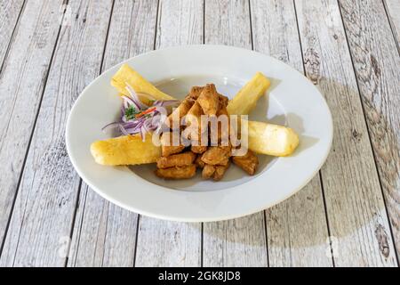 Recette latine pour le chicherron de poisson avec oignon violet cru et yucca frit sur une assiette blanche Banque D'Images