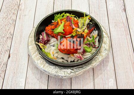 Bol en fonte chaud avec poulet tandoori rouge braisé garni de laitue, d'oignons et de tomates cerises sur table blanche Banque D'Images