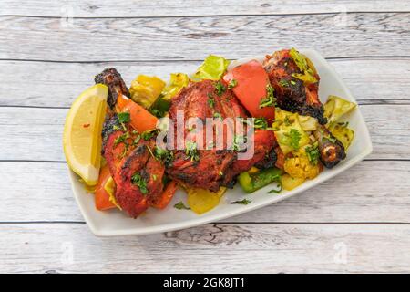 Morceaux de poulet cuits avec une recette tandoori avec beaucoup de persil et de coriandre et garni d'oignon, de poivrons et de citron sur une assiette blanche Banque D'Images