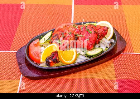 Cuisse de poulet grillée de style hindou tandoori avec une couleur rouge vif et des marques de gril Charred sur la plaque chauffante et la table orange Banque D'Images