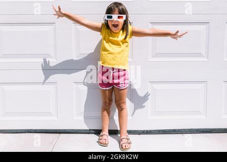 Jolie fille gaie dans des vêtements colorés et décontractés et des verres tridimensionnels debout sur fond de mur blanc Banque D'Images