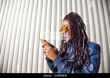 Femme voyageur avec des cheveux bleus et tatouages portant un chapeau et des lunettes de soleil assis près de la caravane dans les bois et regardant l'appareil photo Banque D'Images