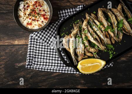 Vue de dessus de savoureux anchois frits avec morceau de citron juteux et persil haché sur le plateau avec sauce salée Banque D'Images