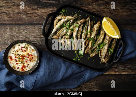 Vue de dessus de savoureux anchois frits avec morceau de citron juteux et persil haché sur le plateau avec sauce salée Banque D'Images