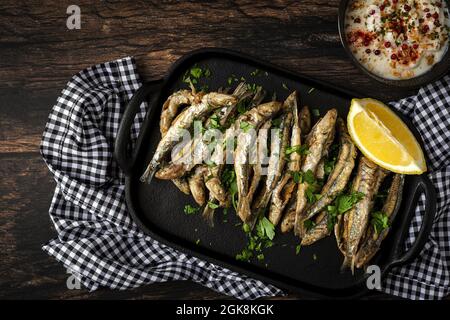 Vue de dessus de savoureux anchois frits avec morceau de citron juteux et persil haché sur le plateau avec sauce salée Banque D'Images