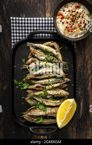 Vue de dessus de savoureux anchois frits avec morceau de citron juteux et persil haché sur le plateau avec sauce salée Banque D'Images