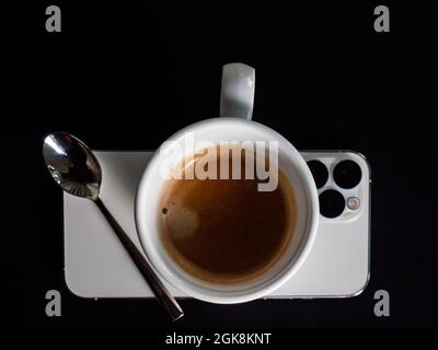 Vue de dessus d'une tasse d'espresso et d'une cuillère en métal placée sur un téléphone mobile moderne sur fond noir Banque D'Images