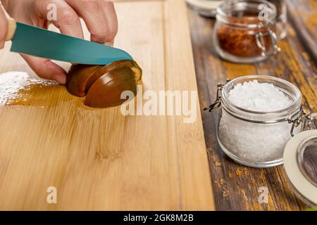 Les mains du chef coupent une paire de tomates kumato en préparant une salade avec des flocons de sel de mer et du paprika Banque D'Images