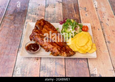 assiette fantastique de côtes de porc avec un petit récipient rempli de sauce barbecue, garniture de laitue et de délicieux frites sur table en bois Banque D'Images