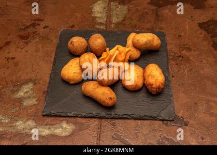 dessus de croquettes assorties fraîchement frites dans une friteuse servie sur une plaque en ardoise noire et sur fond brun métallique Banque D'Images