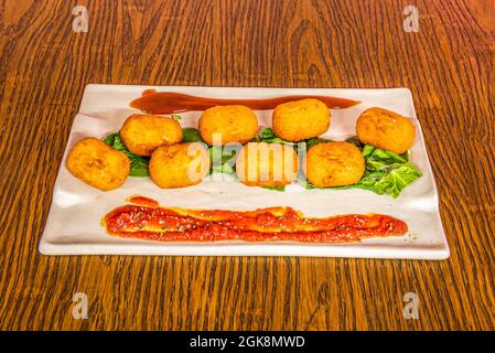 servir des croquettes de morue sur une assiette rectangulaire blanche accompagnée de laitue et de quelques sauces à tremper sur une table sombre Banque D'Images