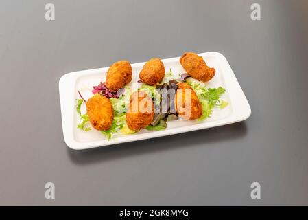 Recette de croquettes de jambon typiquement espagnol sur un plateau blanc avec décoration de laitue et sur une table grise Banque D'Images