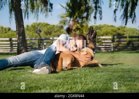 Jeune homme barbu dans des lunettes de soleil couchée sur la prairie contre le chien de race dans le parc le jour d'été Banque D'Images