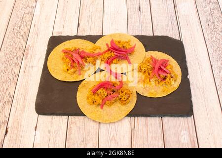 Quatre tacos de cochinita pibil avec tortillas de maïs et oignon rouge sur une plaque d'ardoise noire Banque D'Images