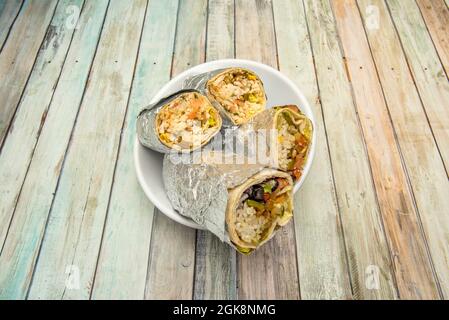 bol blanc avec grandes moitiés de maxi burritos de différentes variantes sur table en bois Banque D'Images