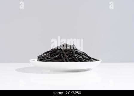 Studio minimaliste avec spaghetti à l'encre noire calmar dans un bol en céramique sur une table blanche Banque D'Images