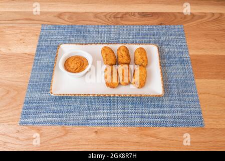 Croquettes de jambon ibérique crémeuses accompagnées de sauce trempée sur une nappe bleue et sur une table en bois Banque D'Images