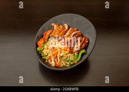 Excellente recette pour le riz frit avec du canard et des légumes sautés dans le wok sur un bol noir et une table sombre Banque D'Images