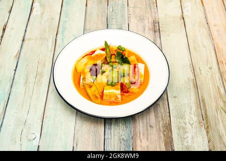 Curry rouge thaï épicé au tofu et aux fruits sur une plaque de métal émaillée blanche et un bord bleu Banque D'Images